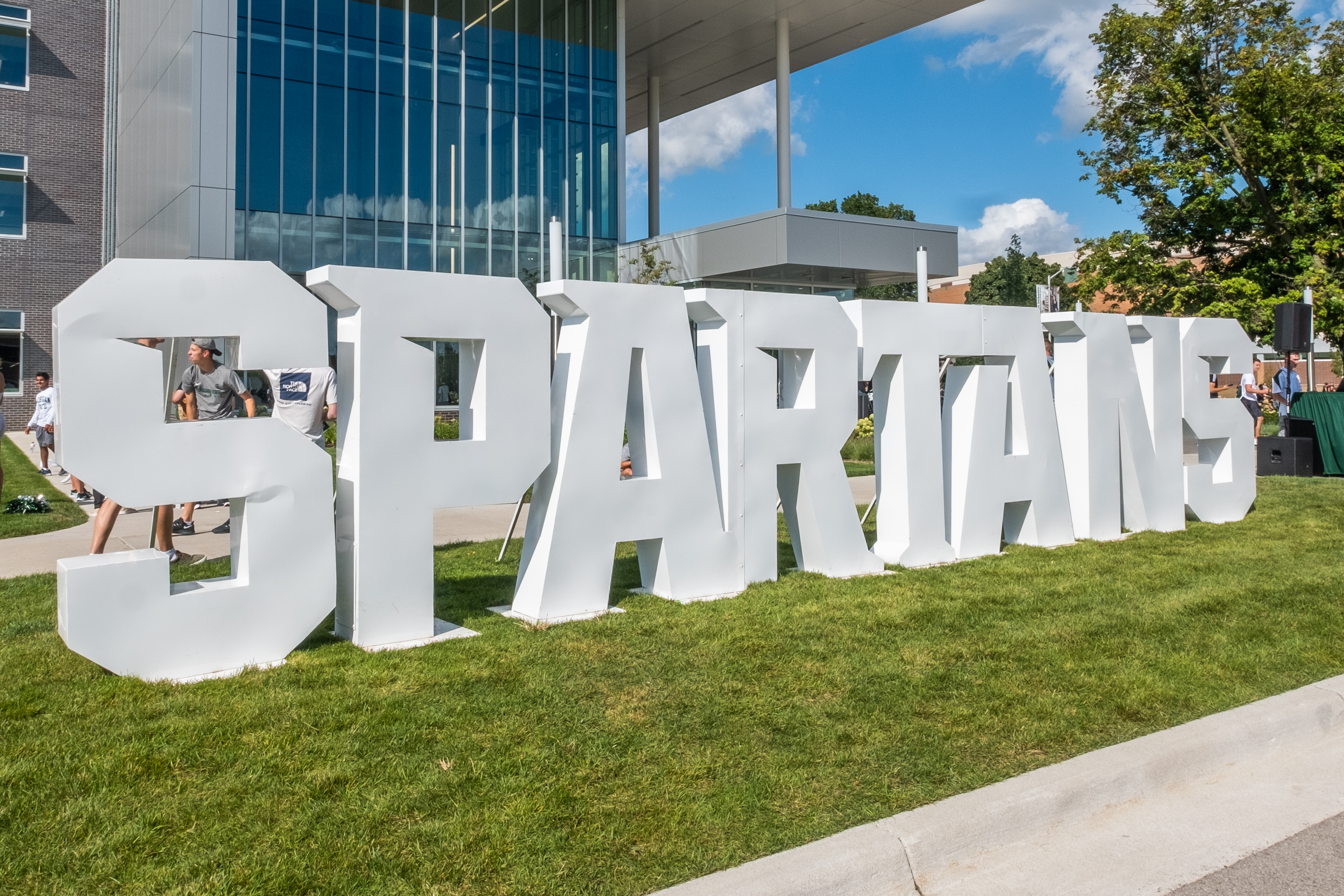 Image of the word "Spartans" in large3 foot white letters set up on the lawn outside on a sunny day. 